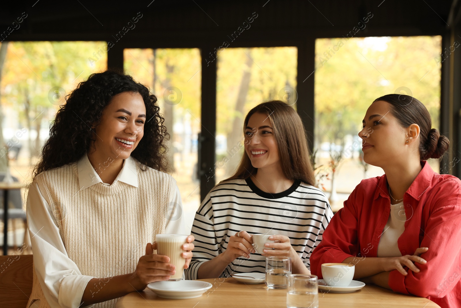 Photo of Happy women with coffee drinks chatting in cafe