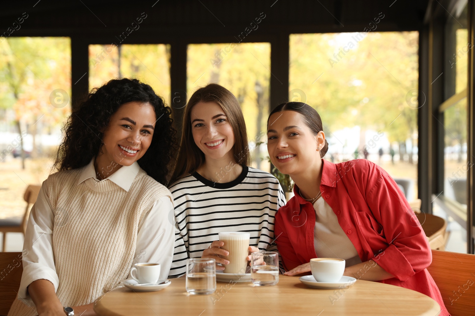 Photo of Happy women with coffee drinks at table in cafe