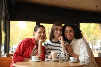 Photo of Happy women with coffee drinks at table in cafe