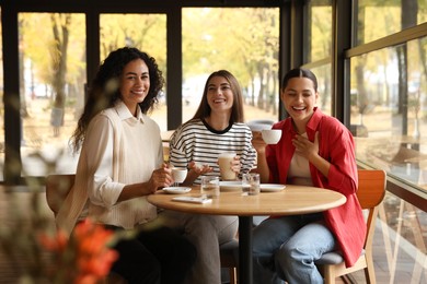 Photo of Happy women with coffee drinks at table in cafe