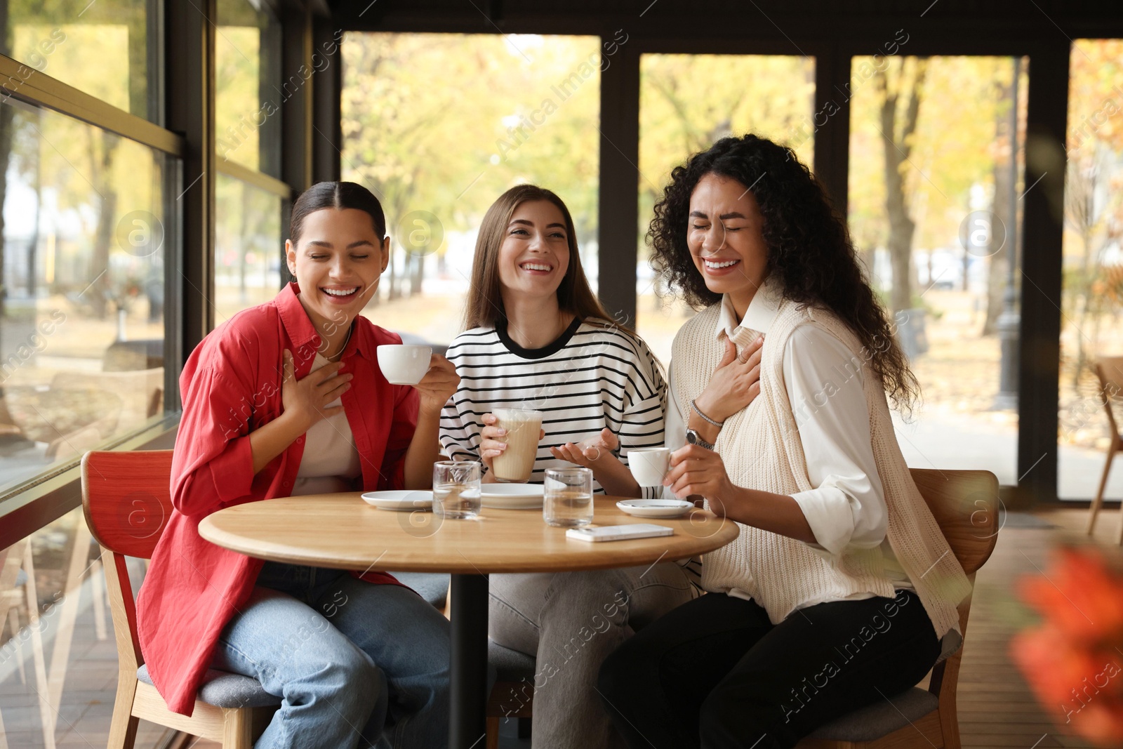 Photo of Happy women with coffee drinks at table in cafe