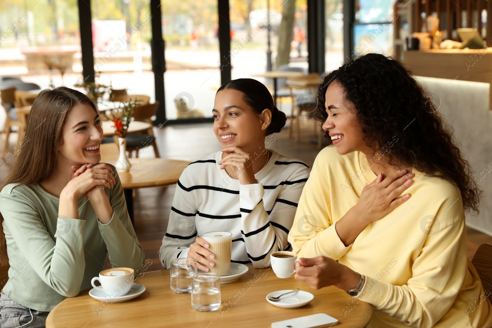 Photo of Happy women with coffee drinks chatting in cafe