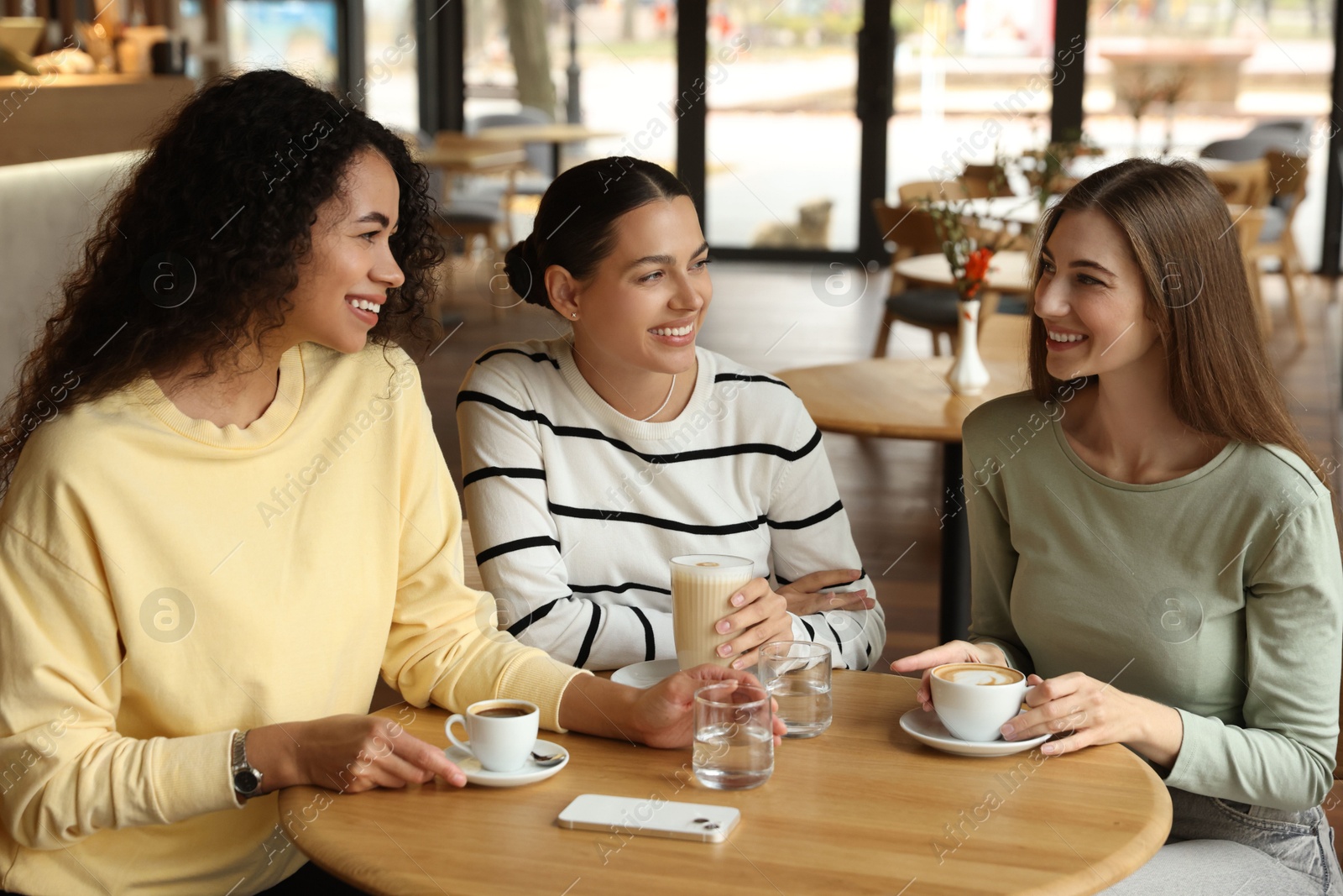 Photo of Happy women with coffee drinks chatting in cafe