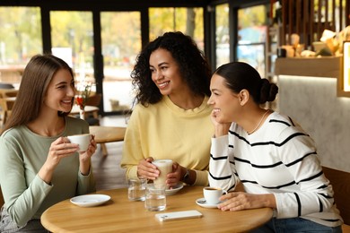 Photo of Happy women with coffee drinks chatting in cafe