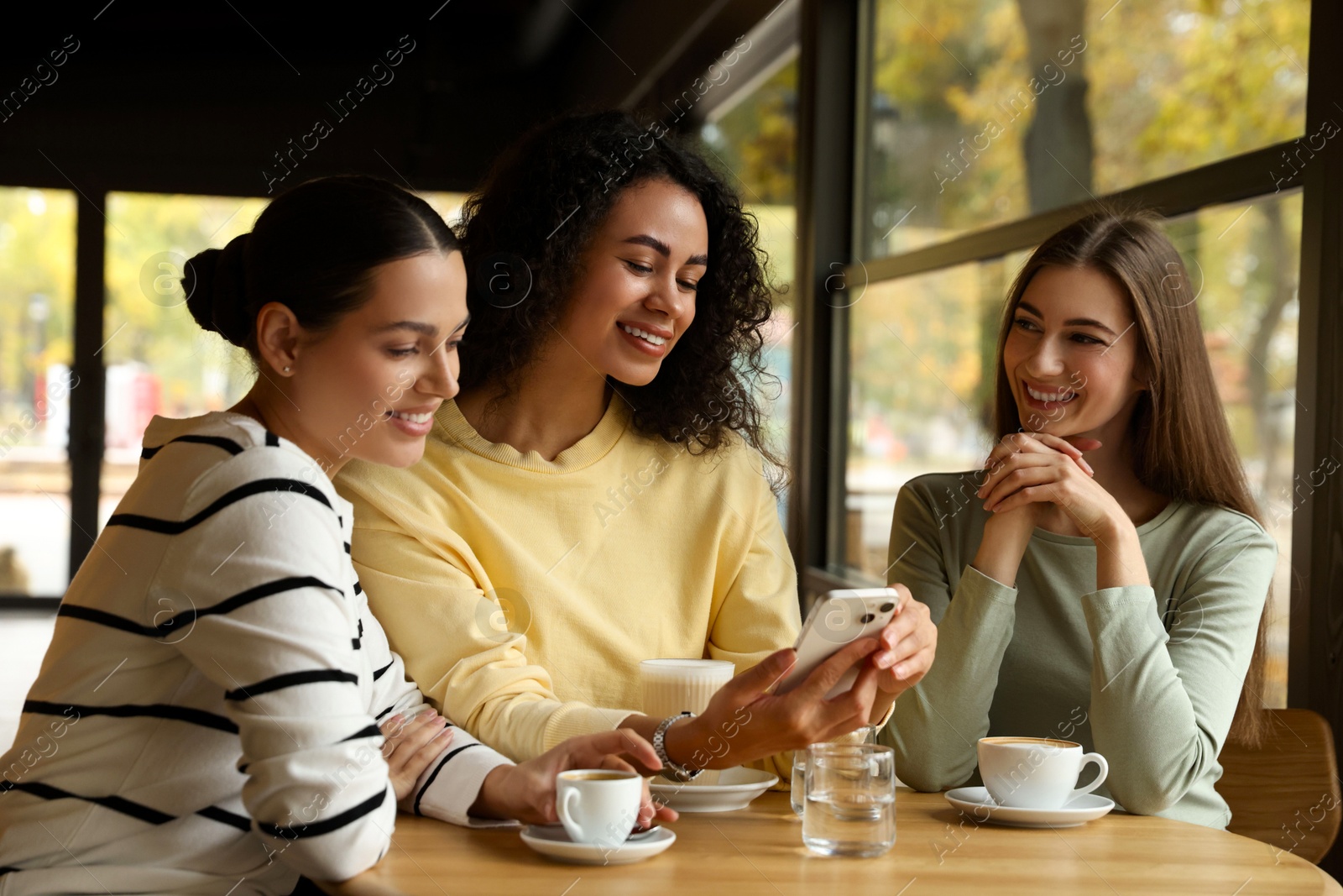 Photo of Woman using smartphone while having coffee with her friends in cafe