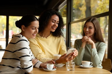 Photo of Woman using smartphone while having coffee with her friends in cafe