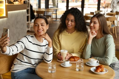 Photo of Happy friends taking selfie during coffee meeting in cafe