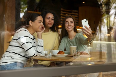 Photo of Women taking selfie at coffee meeting in cafe, view through window