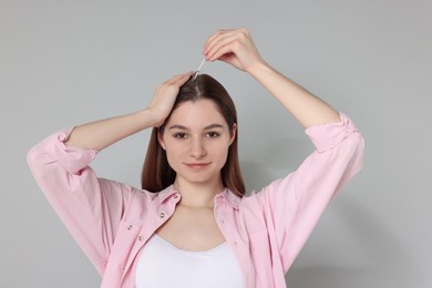 Photo of Hair loss problem. Girl applying serum onto hairline on grey background