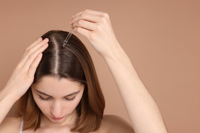 Photo of Hair loss problem. Girl applying serum onto hairline on beige background, closeup