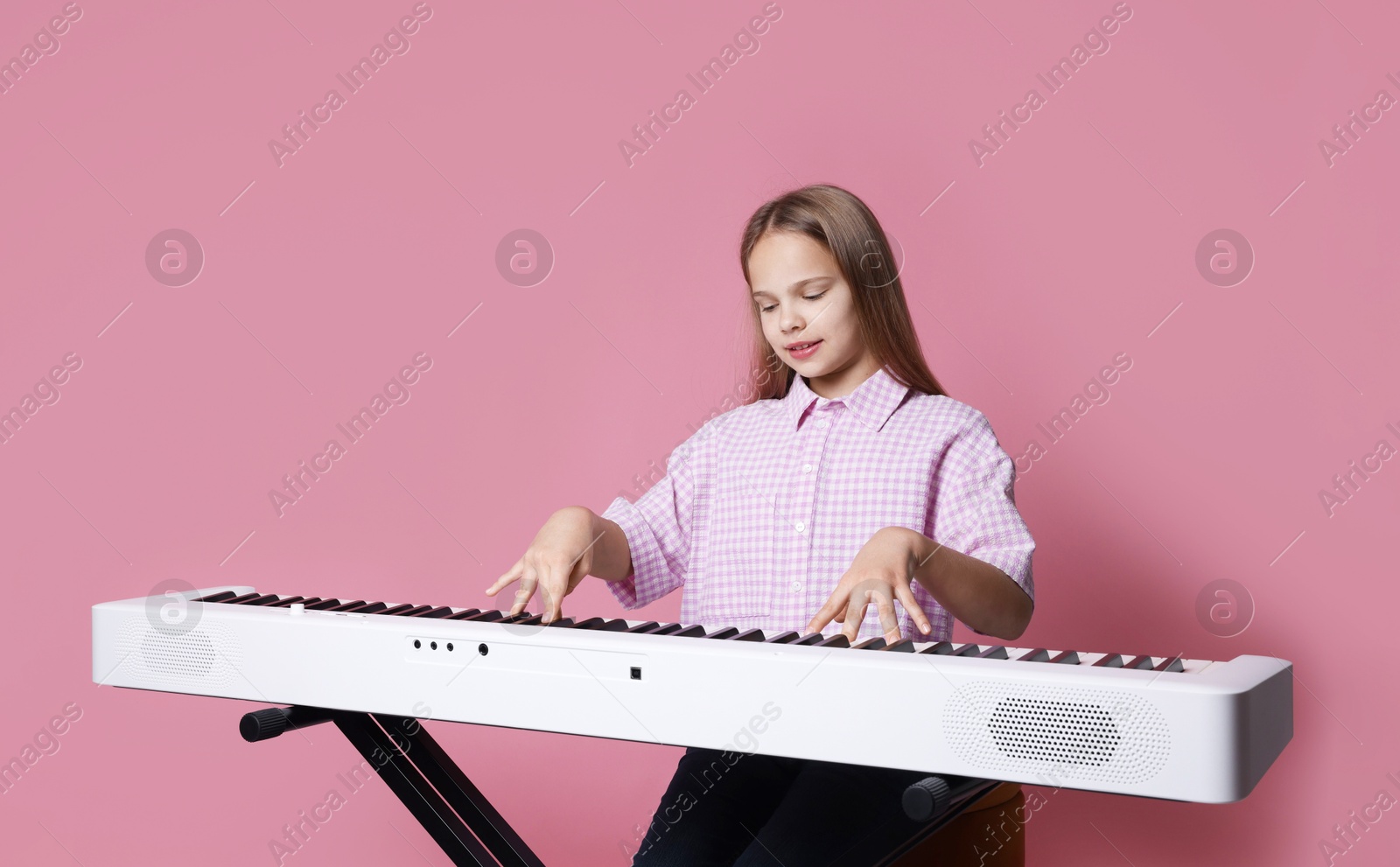 Photo of Cute girl playing synthesizer on pink background