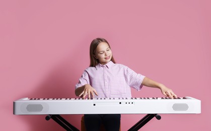 Photo of Cute girl playing synthesizer on pink background