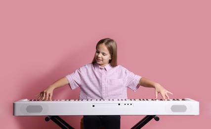 Photo of Cute girl playing synthesizer on pink background