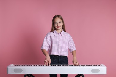 Photo of Cute girl playing synthesizer on pink background