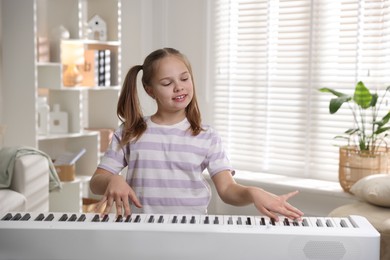 Photo of Cute girl playing synthesizer at home. Electronic musical instrument