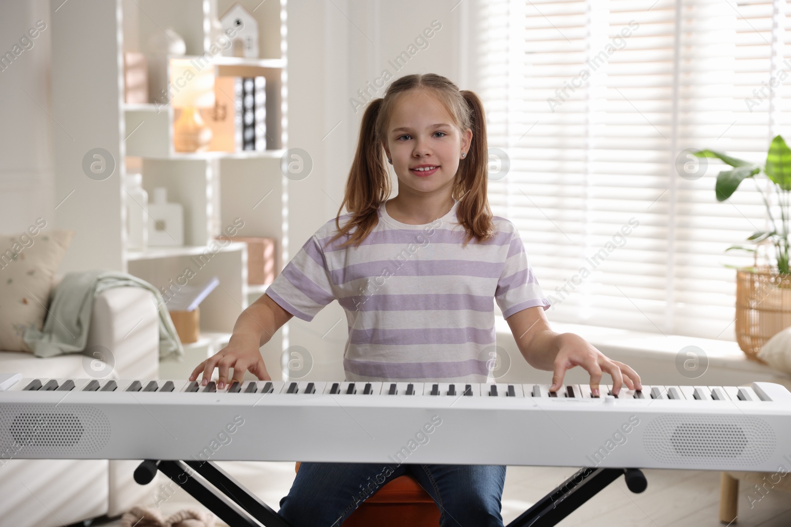 Photo of Cute girl playing synthesizer at home. Electronic musical instrument