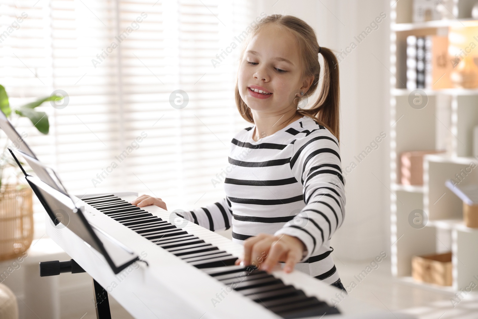 Photo of Cute girl playing synthesizer at home. Electronic musical instrument