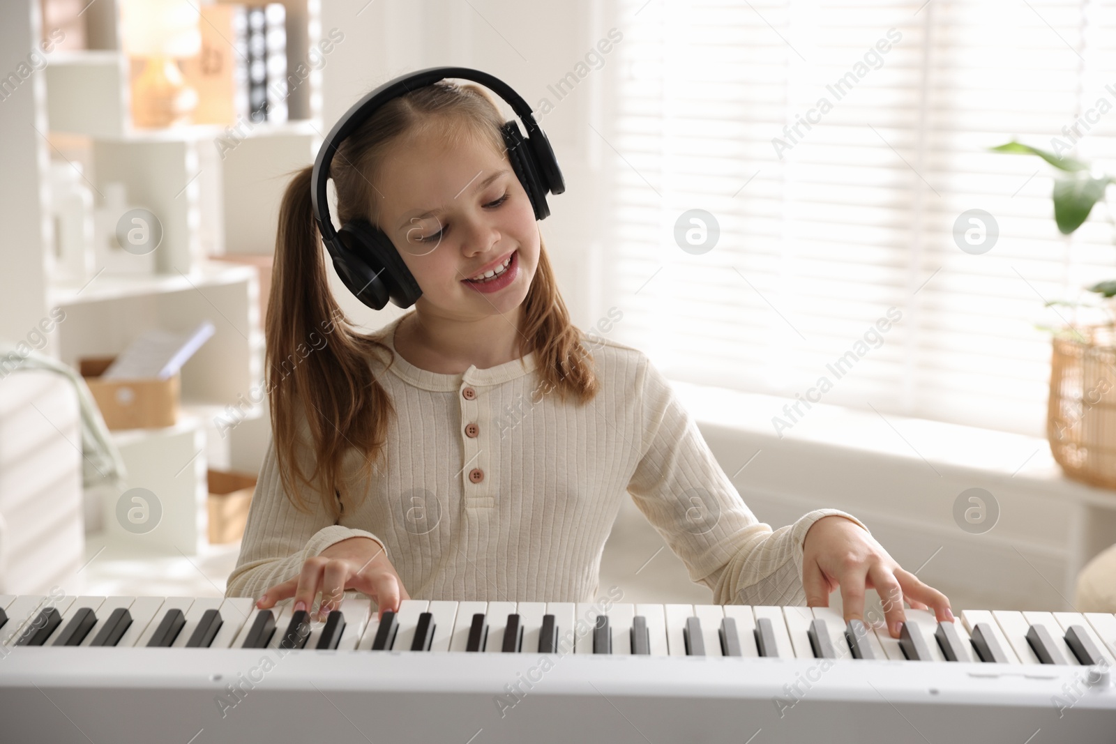 Photo of Cute girl in headphones playing synthesizer at home