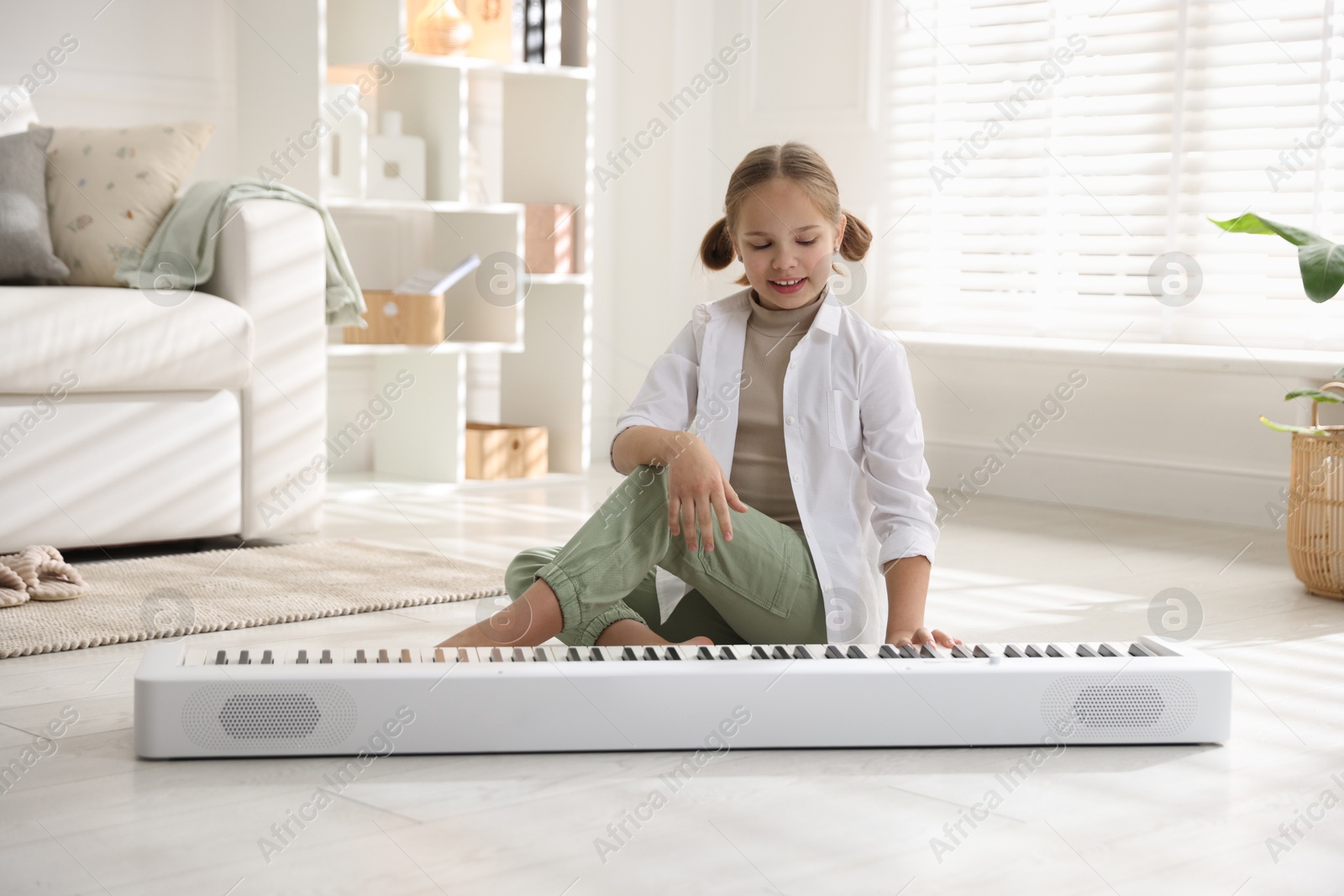 Photo of Cute girl playing synthesizer on floor at home