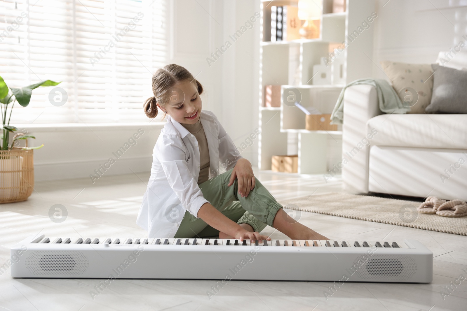 Photo of Cute girl playing synthesizer on floor at home