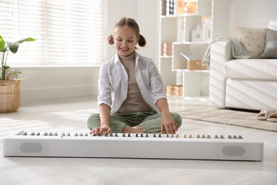 Photo of Cute girl playing synthesizer on floor at home