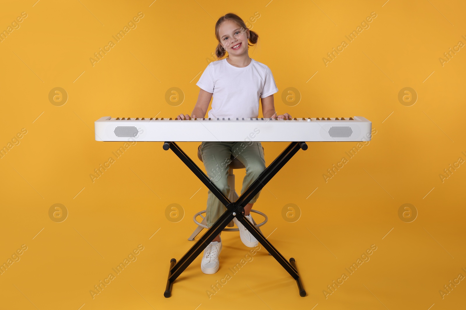 Photo of Cute girl playing synthesizer on orange background