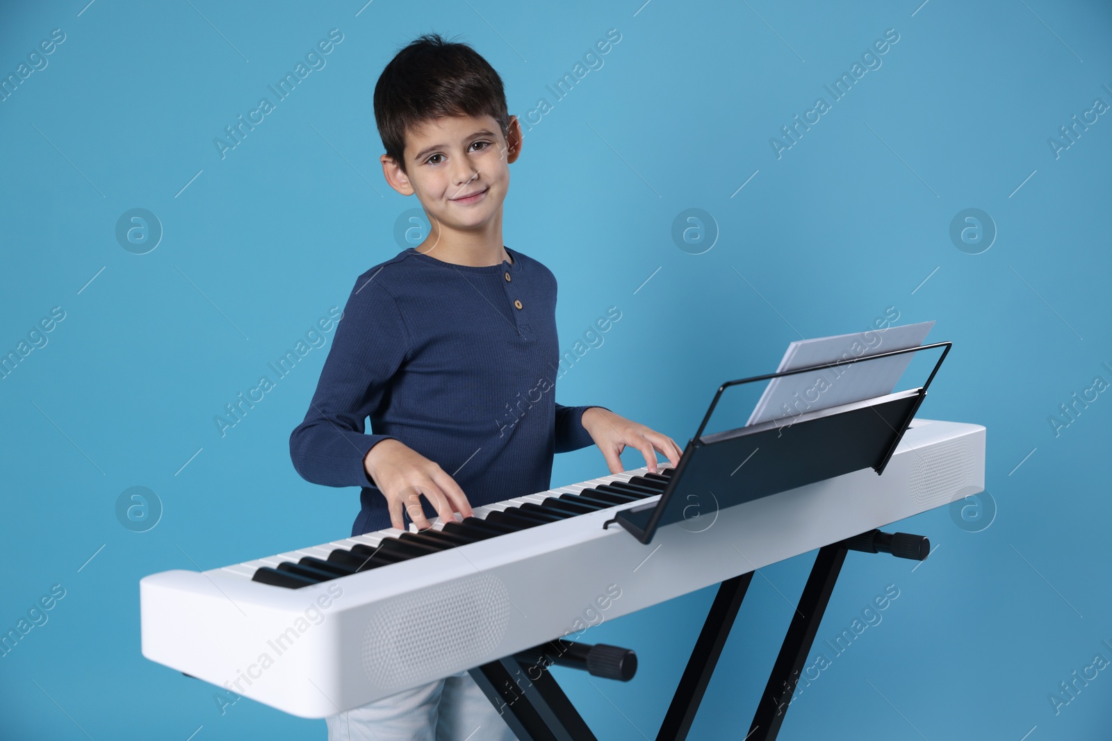 Photo of Cute boy playing synthesizer on light blue background