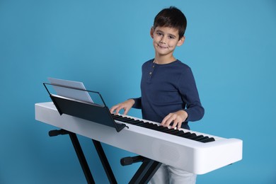 Photo of Cute boy playing synthesizer on light blue background