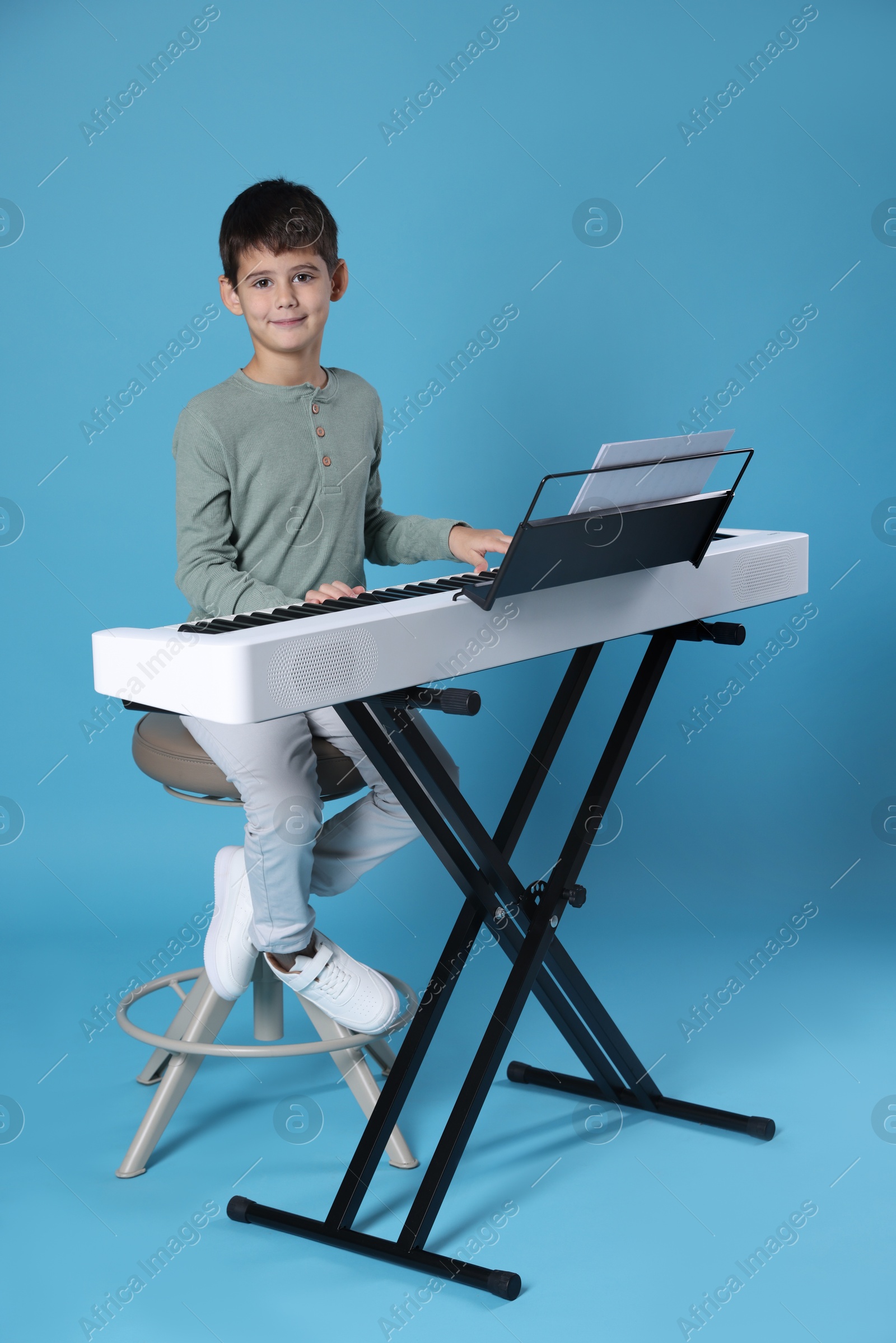 Photo of Cute boy playing synthesizer on light blue background