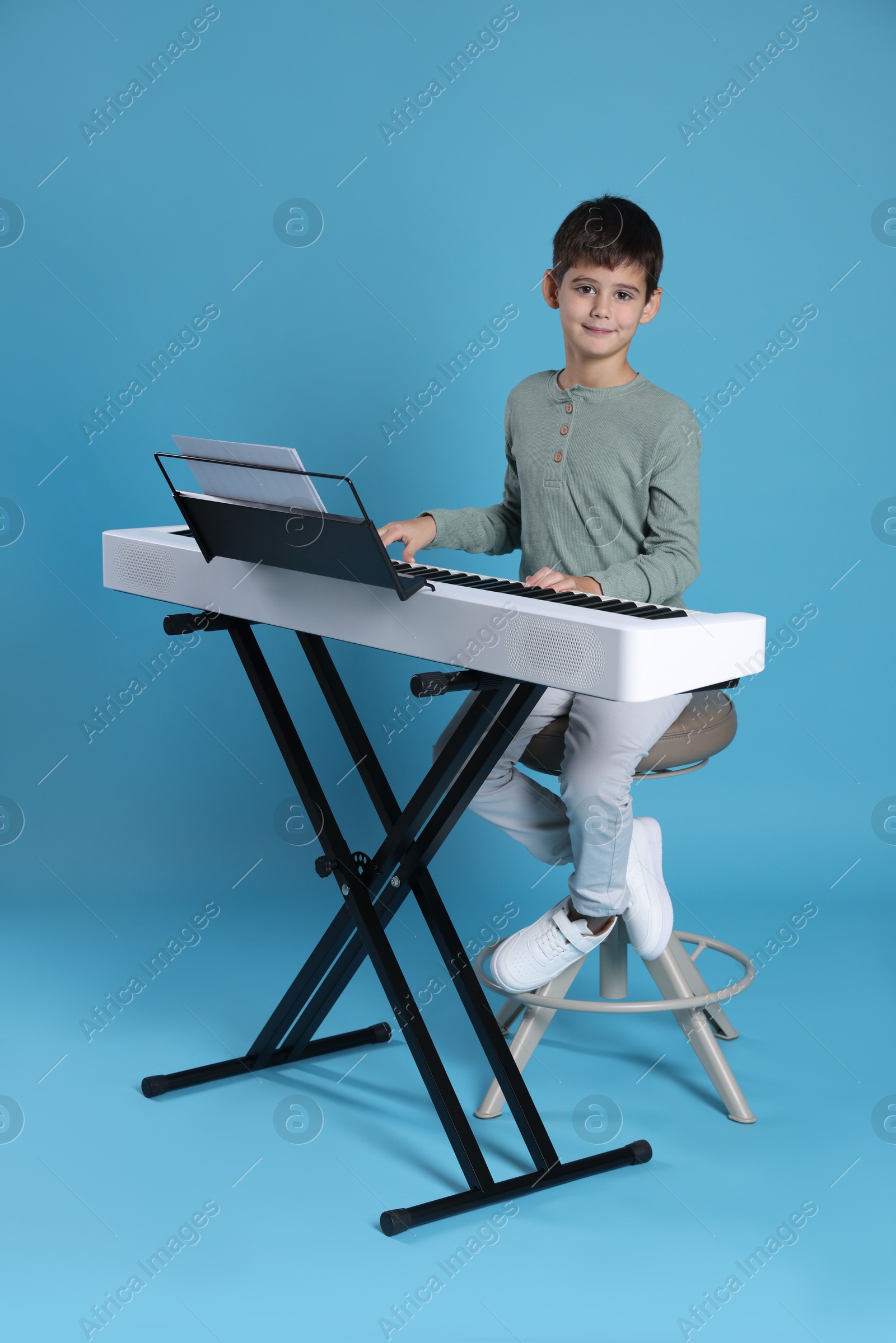 Photo of Cute boy playing synthesizer on light blue background