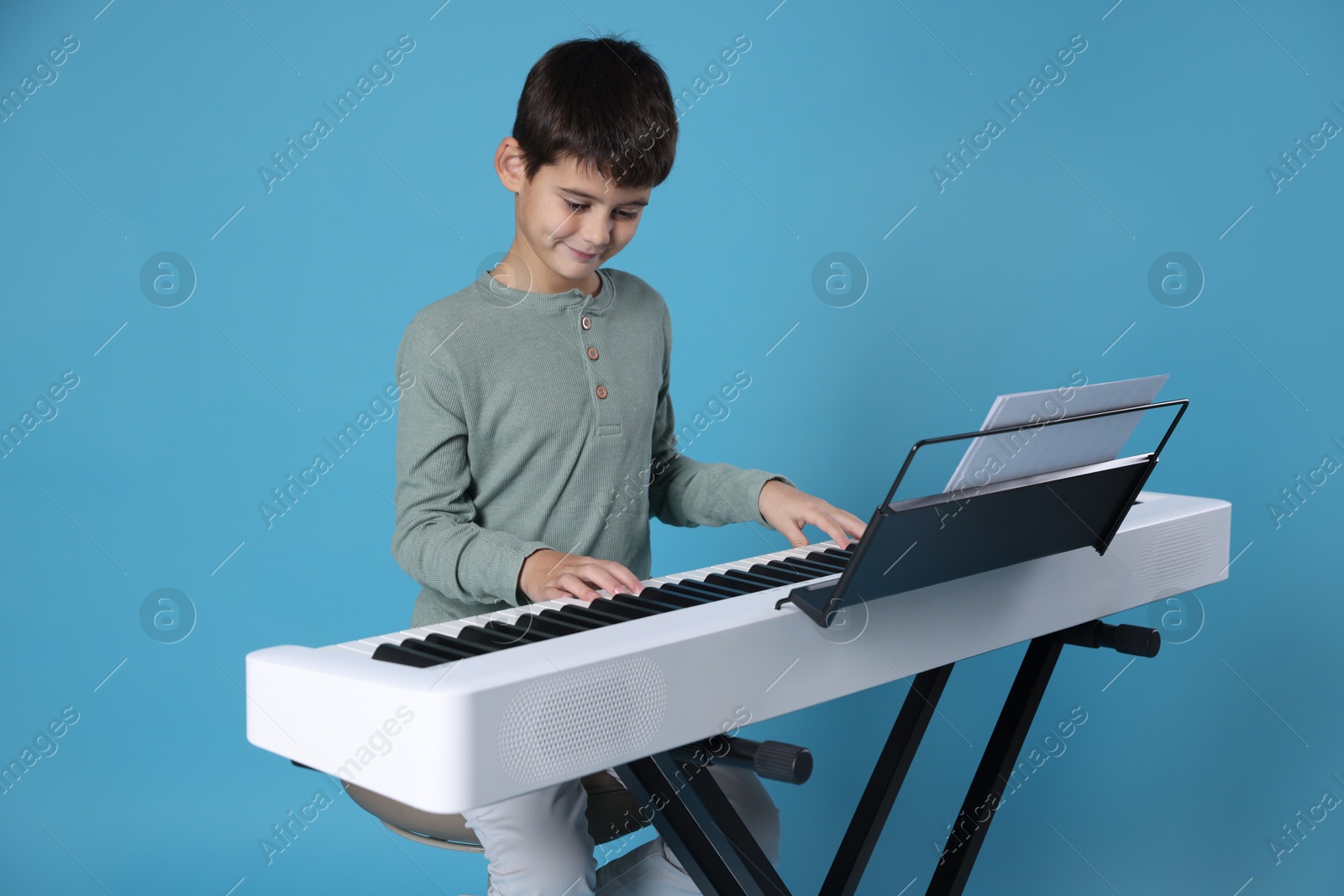 Photo of Cute boy playing synthesizer on light blue background