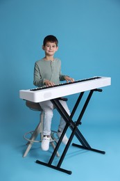 Photo of Cute boy playing synthesizer on light blue background