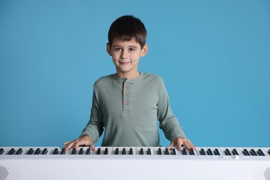 Photo of Cute boy playing synthesizer on light blue background