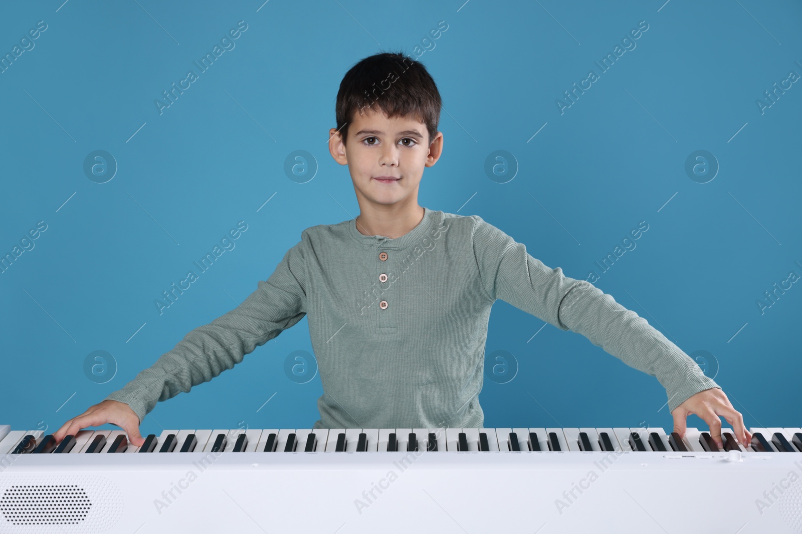 Photo of Cute boy playing synthesizer on light blue background