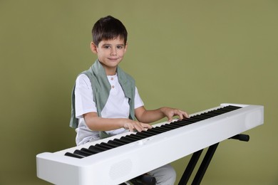 Photo of Cute boy playing synthesizer on olive background