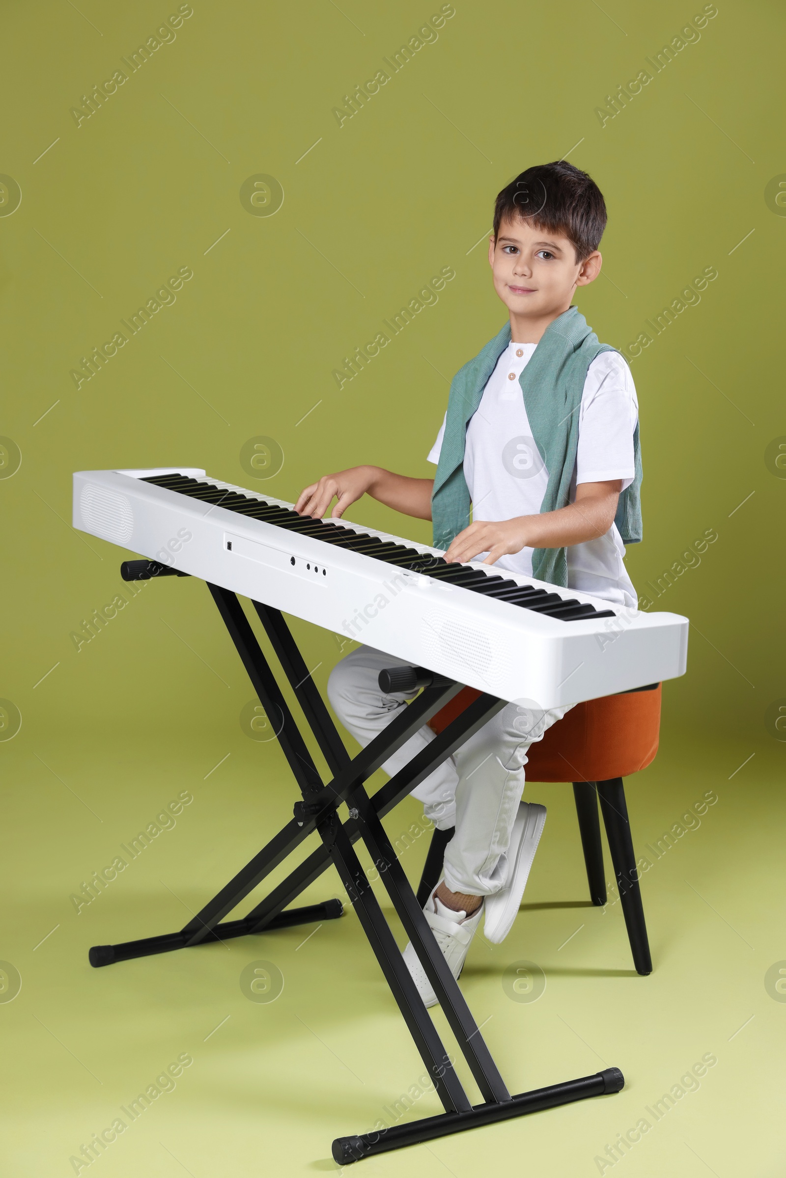 Photo of Cute boy playing synthesizer on olive background