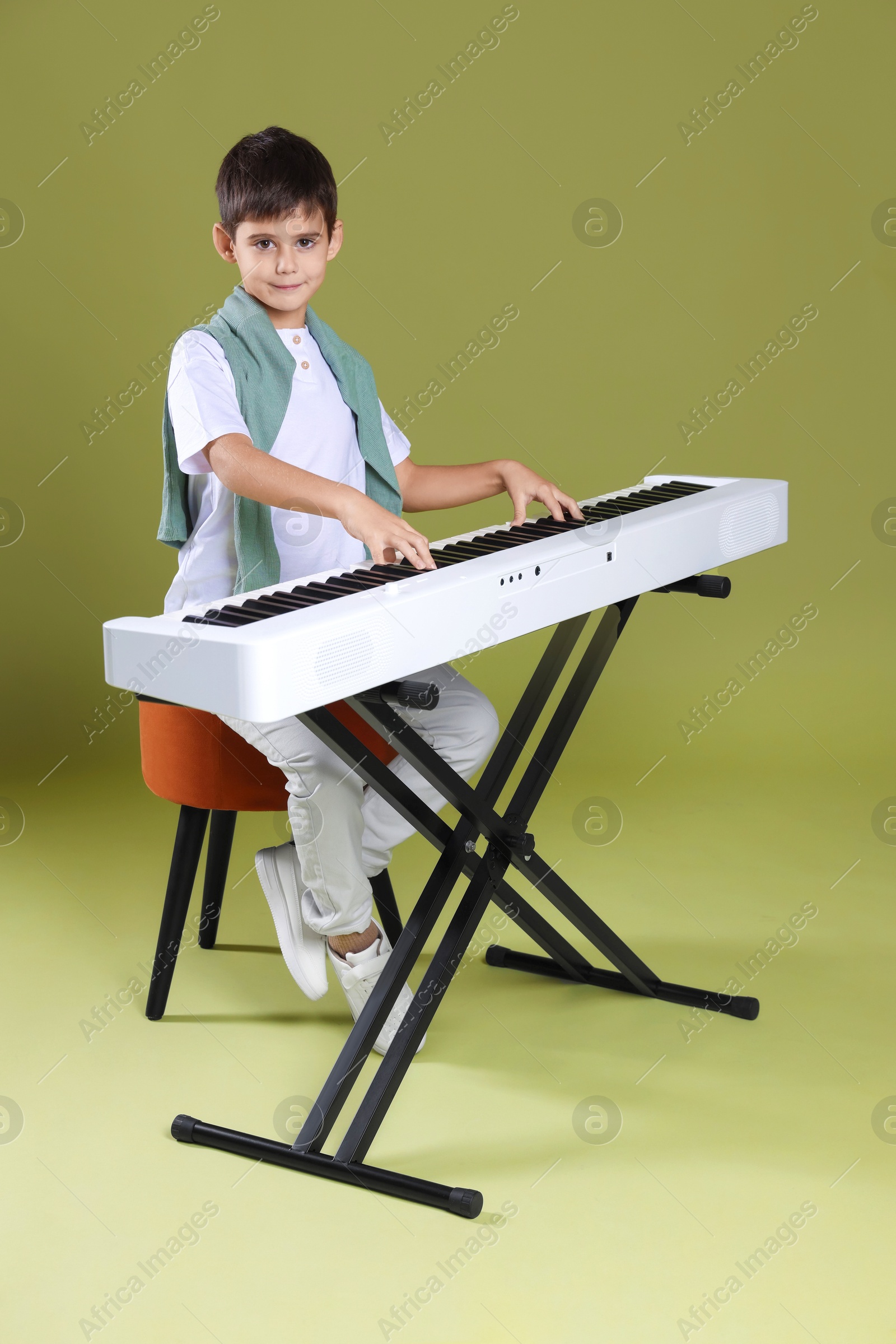 Photo of Cute boy playing synthesizer on olive background