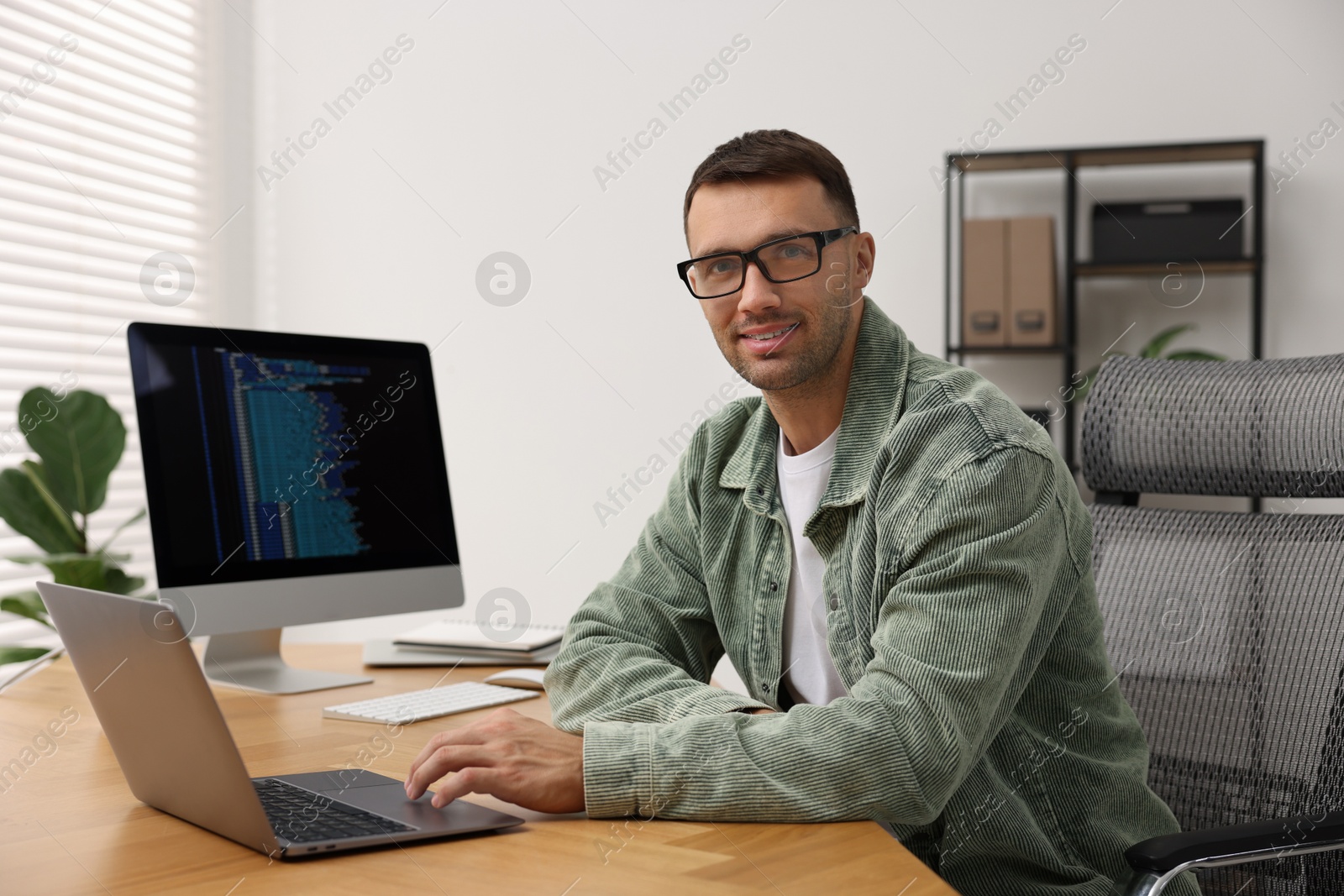 Photo of Programmer working on laptop at wooden desk indoors