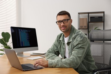 Photo of Programmer working on laptop at wooden desk indoors