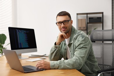 Photo of Programmer working on laptop at wooden desk indoors