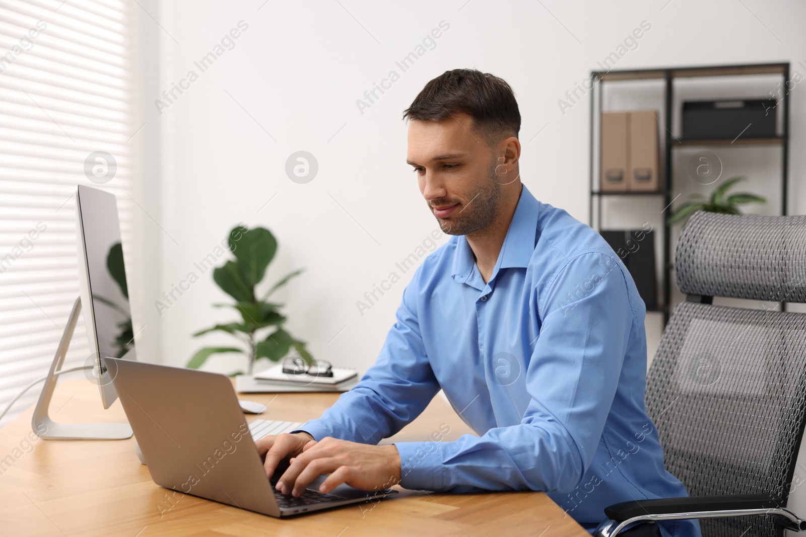 Photo of Programmer working on laptop at wooden desk indoors