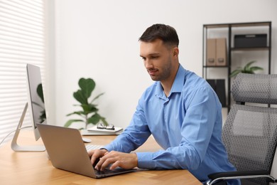 Photo of Programmer working on laptop at wooden desk indoors