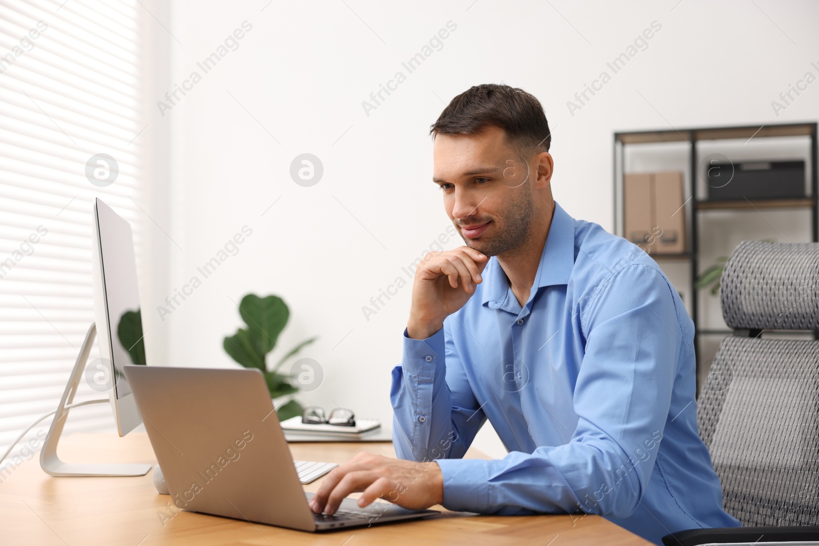 Photo of Programmer working on laptop at wooden desk indoors