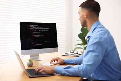 Photo of Programmer working on laptop and computer at wooden desk indoors