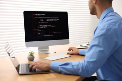 Photo of Programmer working on laptop and computer at wooden desk indoors, closeup