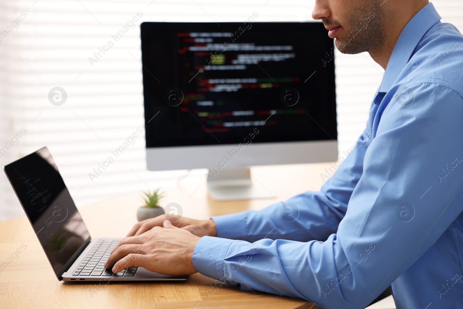 Photo of Programmer working on laptop and computer at wooden desk indoors, closeup