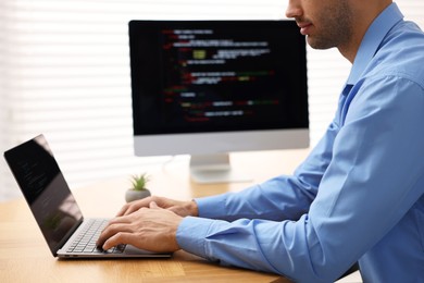 Photo of Programmer working on laptop and computer at wooden desk indoors, closeup