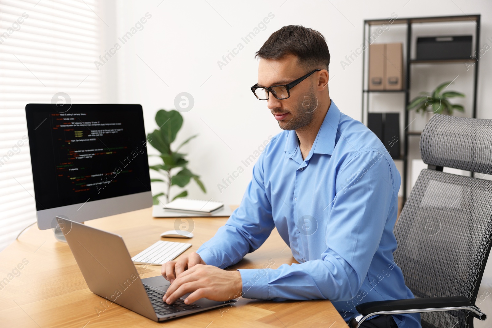 Photo of Programmer working on laptop at wooden desk indoors