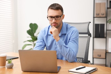 Photo of Programmer working on laptop at wooden desk indoors