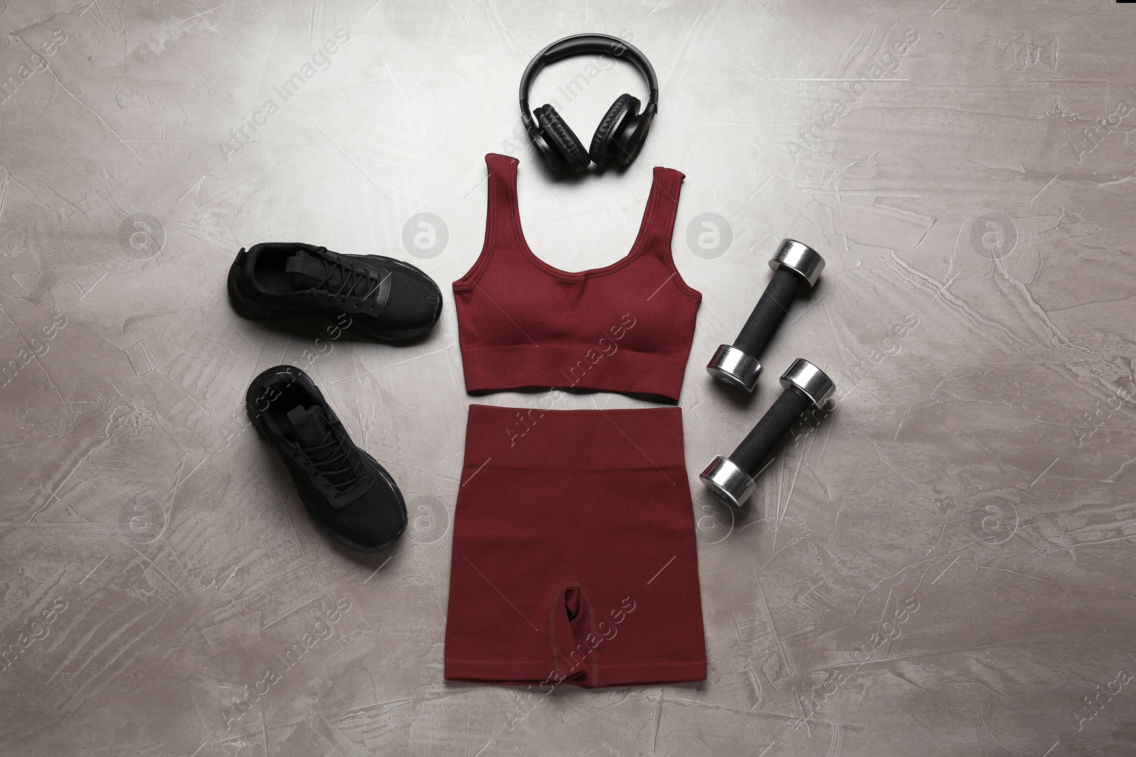 Photo of Brown sportswear, black sneakers, dumbbells and headphones on gray textured background, flat lay